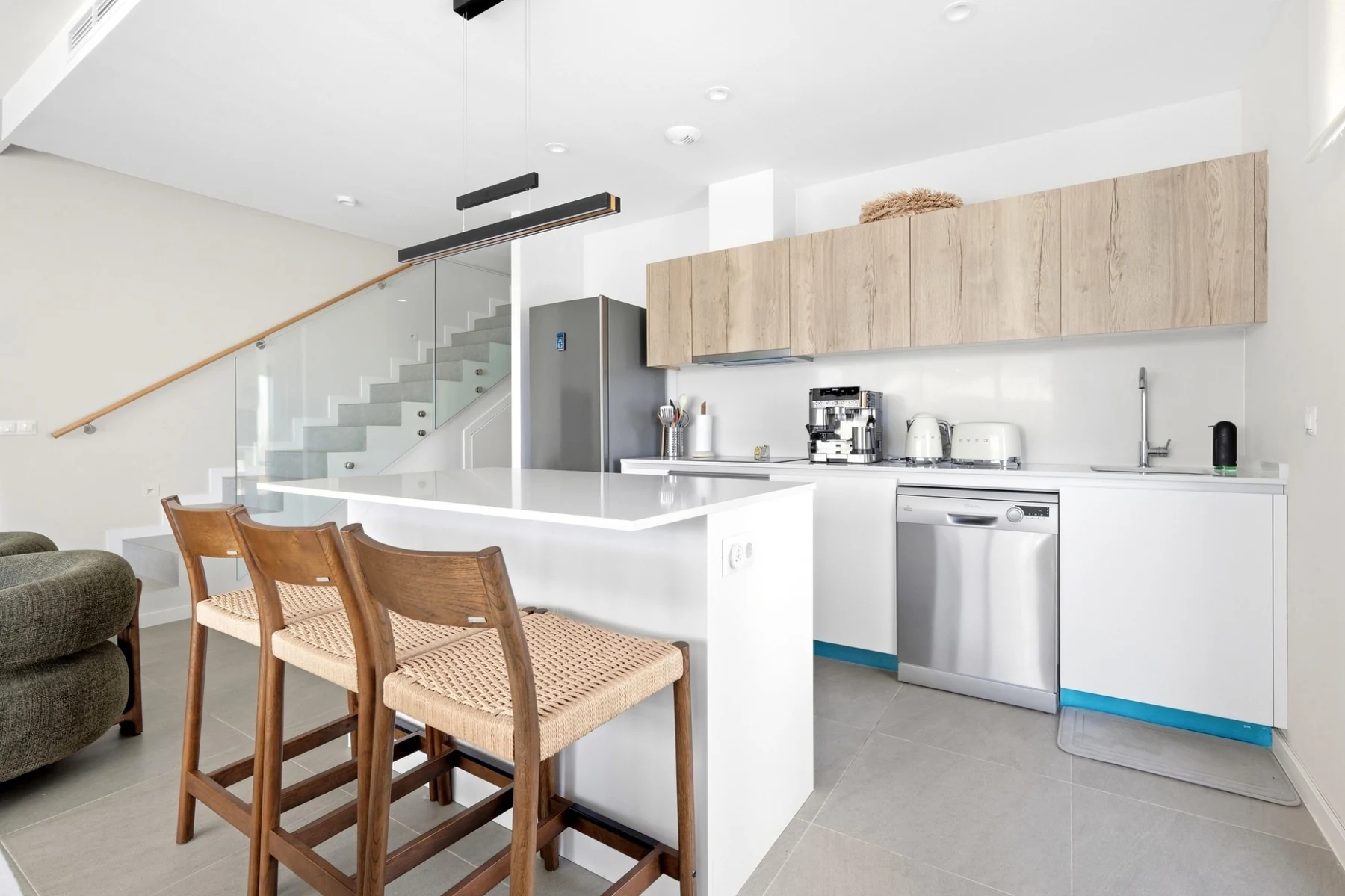 Cocina abierta con barra y escalera acristalada en una vivienda de Mijas