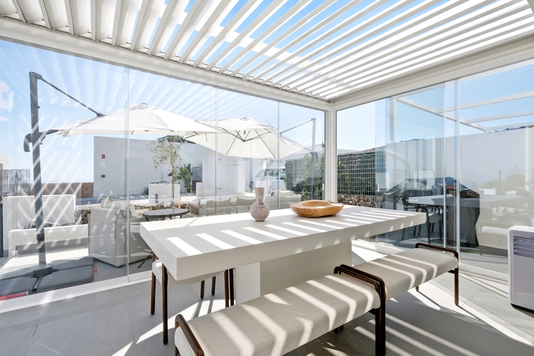 Comedor en terraza acristalada bajo una pérgola de lamas en Mijas