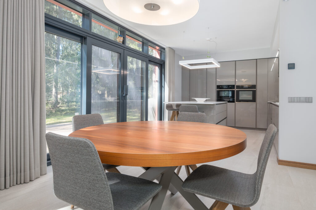 Comedor moderno con mesa redonda de madera, cocina abierta de diseño minimalista y grandes ventanales que aportan luz natural