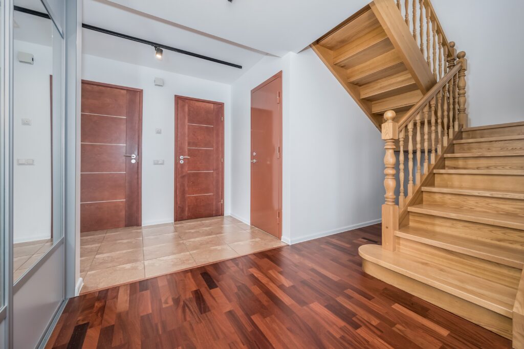 Fotografía inmobiliaria de entrada amplia con escalera de madera y suelo de parquet
