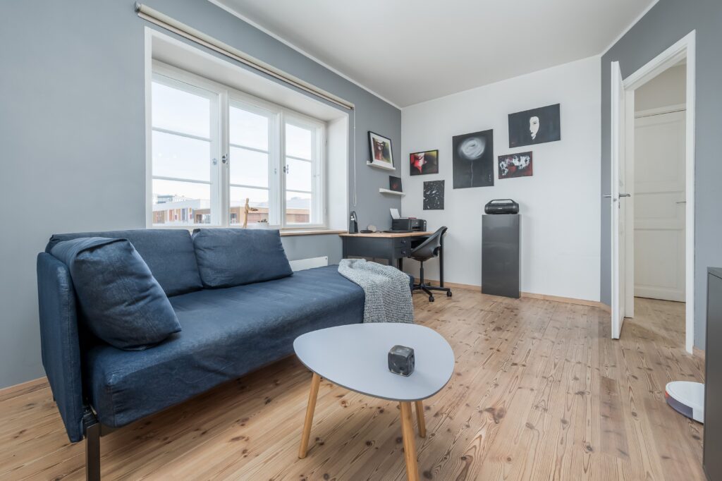 Salón moderno con sofá azul, luz natural y espacio de trabajo integrado en fotografía inmobiliaria profesional